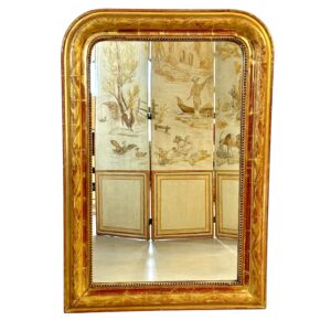 This exquisite French Louis Philippe mirror dates from the mid-19th century, around 1850, and exemplifies the elegant simplicity characteristic of the Louis Philippe period. The frame features rounded upper corners and a rectangular silhouette, enhanced by its rich gold leaf finish over red bole. Subtle floral engravings are etched into the gesso, adding a touch of refinement without overpowering the frame’s classic lines. The mirror’s warm patina is accentuated by signs of age and wear, including a few small losses and touch-ups to the gilding, particularly visible on the edges and corners, which have been sympathetically restored in the past. These time-worn details contribute to the mirror’s authentic antique charm and are consistent with its age and provenance. The glass is original, with light foxing and a soft, reflective surface typical of 19th-century mercury-backed mirrors. It is surrounded by a delicate beaded border that adds further depth and definition to the frame. With its understated elegance and generous size, this mirror would suit both classic and contemporary interiors. It can be placed above a fireplace, console table, or used as a floor mirror for added dramatic effect. A timeless piece that brings a touch of French sophistication to any space.
