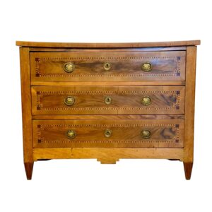 This French commode from the late 18th century is a distinguished example of the Louis XVI style, celebrated for its balance, geometric harmony, and classical inspiration. Crafted in fruitwood with walnut veneer, the piece exemplifies the refined taste of the period, where clean lines replaced the curves of the Rococo era. The façade features three full-length drawers, each adorned with intricate marquetry borders in geometric and checkerboard patterns. This precise inlay work emphasizes the symmetry and order so highly valued in Louis XVI design. The contrasting tones of fruitwood and walnut enhance the natural grain, giving both warmth and visual depth to the commode. Original gilt-bronze escutcheons and ring pulls, finely cast with classical urn motifs, add an elegant neoclassical touch while underlining the commode’s authenticity. The drawers are flanked by a solid frame that extends into tapered legs, typical of the architectural influence of the period. The slightly curved top softens the rectilinear form, adding a subtle sophistication. Combining functionality with elegance, this Louis XVI commode embodies the timeless appeal of French neoclassical furniture. Perfect for refined interiors, it offers both practical storage and the charm of an authentic 18th-century piece, making it a distinguished addition to any collection.