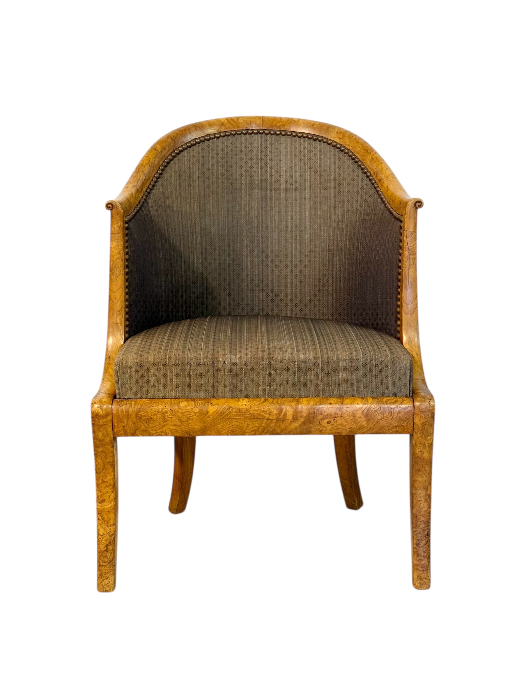 Elegant pair of 19th century French Empire-style armchairs featuring beautifully figured burl wood and a distinctive gondola-shaped back, a form that became emblematic of refined seating during the Empire period. The curved silhouette flows gracefully from the backrest to the gently scrolled arm terminals, creating both visual harmony and comfort. The warm, honey-toned burl wood displays exquisite grain patterns that highlight the craftsmanship and quality of the period. The chairs stand on elegant sabre legs, typical of the Empire aesthetic, adding to their sense of balance and poise. Upholstered in a finely textured fabric with subtle geometric motifs in muted olive-brown tones, they are finished with antique brass nailhead trim outlining the contours of the frame. This sophisticated pair combines neoclassical inspiration with understated luxury, making them an ideal choice for a library, salon, or study. In good antique condition, showing light wear consistent with age and use.